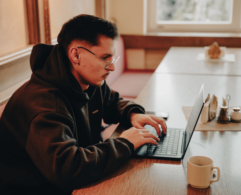 a faculty member of the European Theological Seminary is typing on his computer while having a coffee cup next to it.